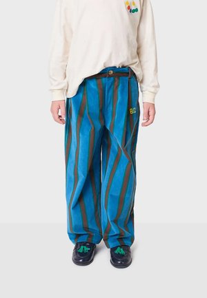 Plave i smeđe prugaste hlače širokih nogavica od teksturirane tkanine sa žutim izvezenim logom. Uparene s krem dugom majicom.