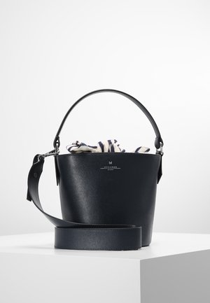 Sac seau en cuir noir avec poignée supérieure et bandoulière large amovible, partiellement rempli d'un tissu rayé à l'intérieur.