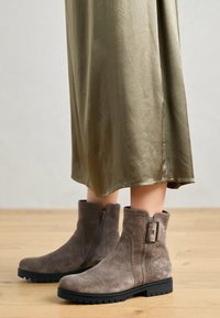 Botas de tobillo de ante en gris con cremallera lateral y detalle de hebilla, que cuentan con una superficie texturizada y suelas de goma negra para mayor tracción.