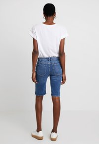 Denim shorts in een middelblauwe, knie-lange uitvoering met een aangesloten tailleband, voorzien van twee achterzakken en opgerolde zomen, gecombineerd met een wit t-shirt.