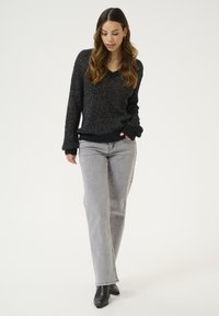 Svart stickad tröja med V-ringning och lös passform, kombinerad med ljusgrå raka jeans och svarta ankelskor.