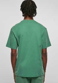 Tricou din bumbac verde, cu mânecă scurtă și croială lejeră. Textură netedă, gât rotund și detaliu cu tiv drept la spate.
