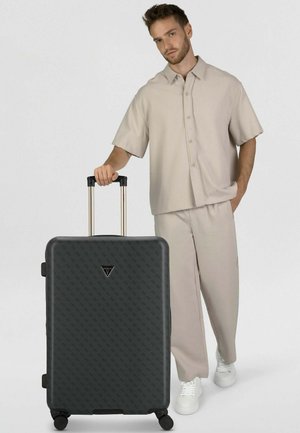 Hartschalen-Koffer aus strukturiertem schwarzem Kunststoff, mit Logo, ausziehbarem goldenem Griff und Rollen für Mobilität.