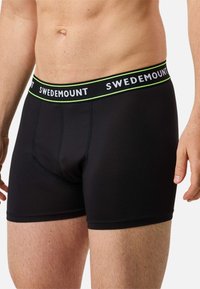Czarne bokserki z dopasowanym krojem, wykonane z gładkiej tkaniny. W pasie znajduje się taśma z napisem "SWEDEMOUNT" w białym kolorze z zielonymi akcentami.