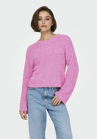 Maglione rosa testurizzato con maniche lunghe e scollatura rotonda, abbinato a jeans a vita alta azzurri. Materiale morbido e accogliente.
