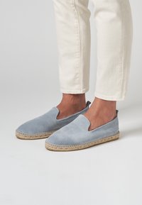 Espadrilles de ante azul claro con puntera cerrada y laterales elásticos, que presentan una suela de cuerda de yute y un detalle de costura a lo largo del borde.
