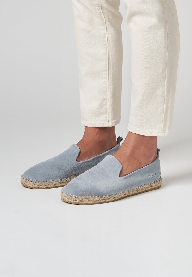 Espadrilles de ante azul claro con puntera cerrada y laterales elásticos, que presentan una suela de cuerda de yute y un detalle de costura a lo largo del borde.