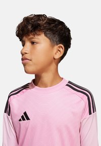 Maglietta sportiva a maniche lunghe rosa con un design testurizzato, dettagli neri a tre strisce sulle spalle e logo Adidas sul lato sinistro del petto.