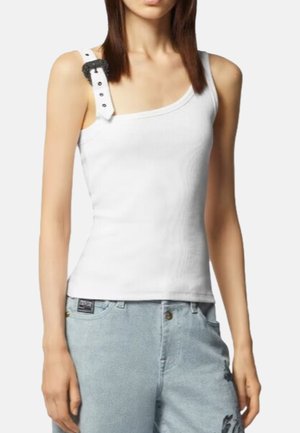 Top in cotone bianco con coste, dal collo asimmetrico, una spalla con un dettaglio a fibbia nera; abbinato a un paio di jeans in denim azzurro chiaro.