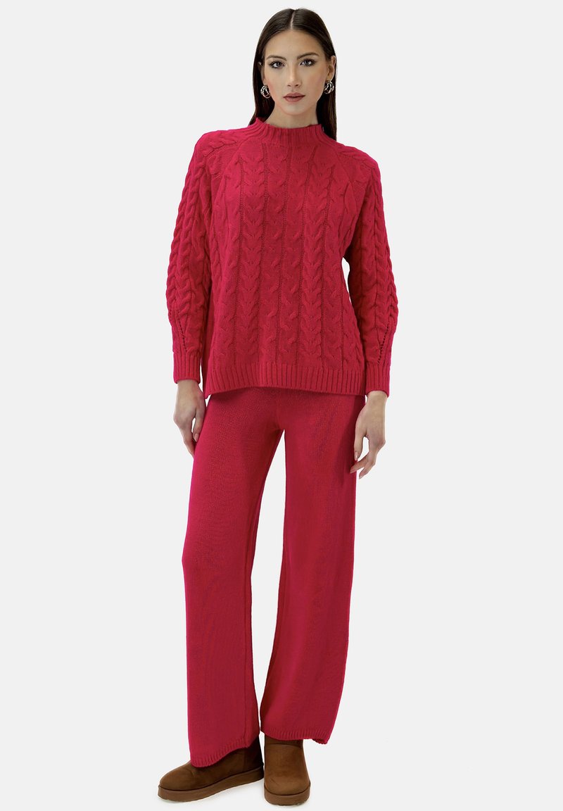 Magenta sweter dzianinowy z wzorem w warkocze i prążkowanym dekoltem, zestawiony z dopasowanymi spodniami o szerokich nogawkach oraz brązowymi botkami za kostkę.