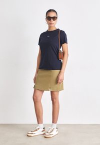 Námornícka tričko s krátkym rukávom, olivovo zelená áčková sukňa, biele a hnedé tenisky a hnedá crossbody taška. Hladká textúra, minimálny dizajn.