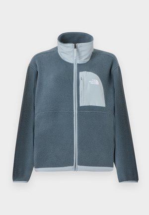 Lyseblå fleecetrøje med fuld lynlås foran og brystlomme med The North Face-logo på højre side.