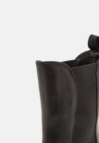 Gros plan sur la tige d'une botte en cuir noir montrant le cuir lisse et un panneau latéral élastique pour un ajustement extensible.