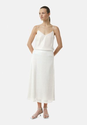 Witte satijnen camisole met dunne bandjes en een bijpassende enkellange rok met een subtiele glans, gecombineerd met zilveren strappy hakken.