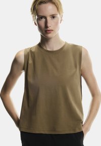 Hnedý bezrukávový top v voľnom strihu, s okrúhlym výstrihom a hladkou textúrou, spárovaný s tmavými nohavicami pre kontrast.