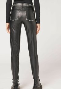 Svarta läderbyxor med en åtsittande design, prydda med dekorativa nitar på bakfickorna och midjebandet, kombinerat med svarta snörstövlar.
