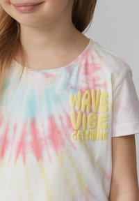 Witte t-shirt met korte mouwen en een meerkleurig tie-dye patroon in roze, geel en blauw. Met 3D gele tekst: "WAVE VIBE GET SHINE."