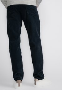 Donkerblauwe corduroy broek met een recht model, voorzien van twee achterzakken en een geribde textuur. Gecombineerd met witte schoenen en een lichtgrijze trui.