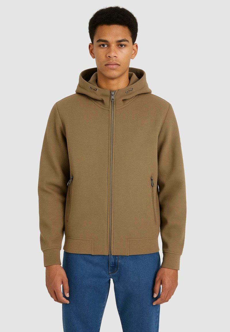 Felpa con zip di colore marrone, a coste, con cappuccio regolabile con cordino, tasche laterali e vestibilità rilassata, abbinata a jeans blu.