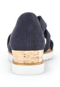 Donkerblauwe suède schoenen met een kurkhoogte en een witte rubberen zool, met een kruiselings bandontwerp en een gladde textuur.