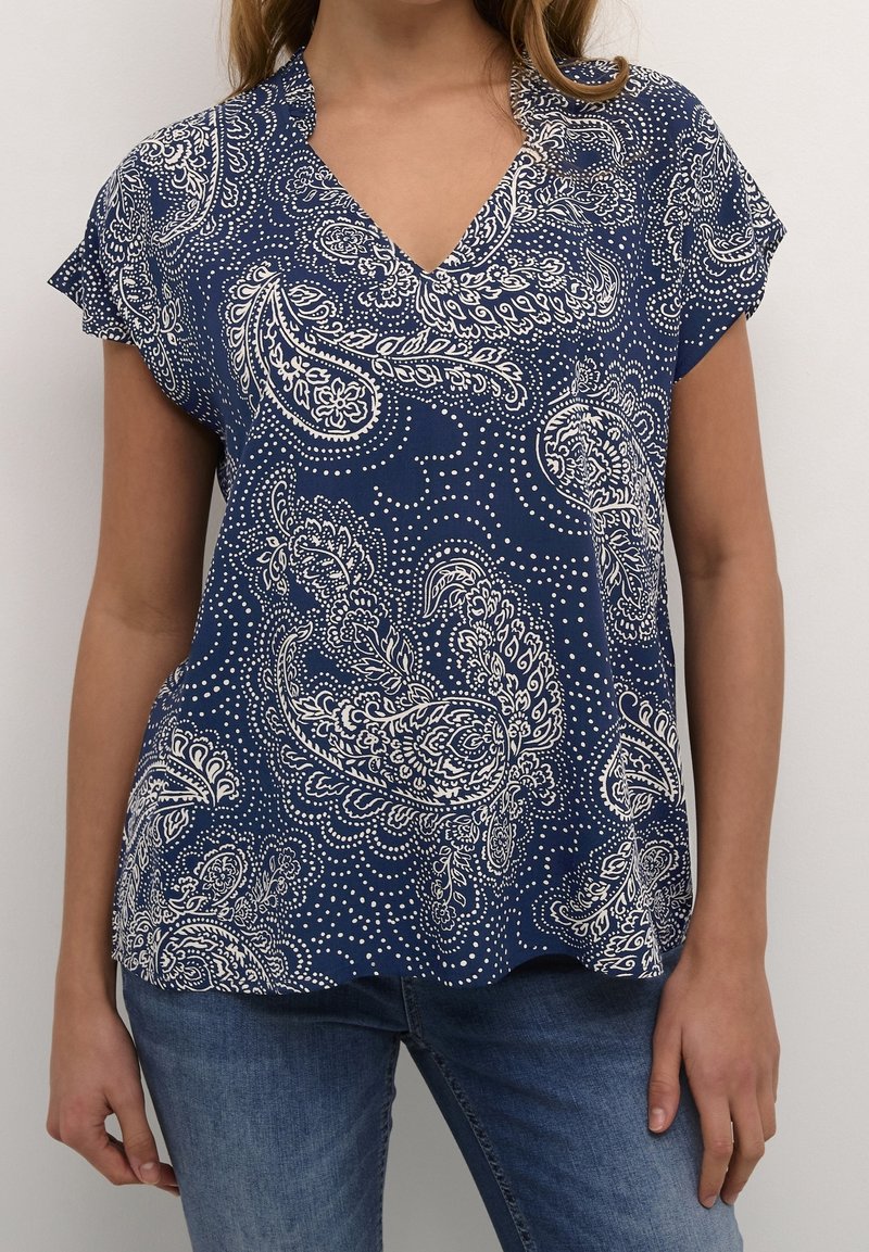 Námořnická modrá blůza s výstřihem do V, krátkými rukávy a bílými paisley vzory. Vyrobena z lehkého materiálu s volným střihem.