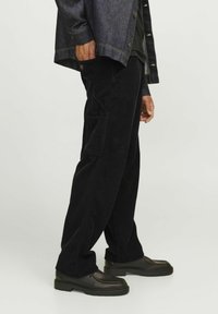 Zwarte corduroybroek met een relaxte pasvorm, voorzien van zijzakken en een gestructureerd oppervlak, gecombineerd met donkere schoenen en een denimjack.