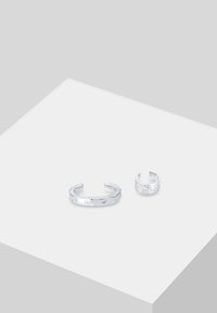 To sølvringer på en lys grå overflade. Den større ring har en glat, poleret overflade, mens den mindre har en tekstureret, hamret design.