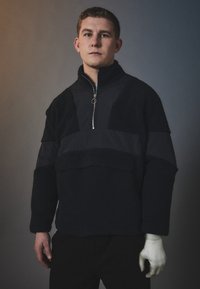 Zwarte fleece pullover met een half-rits kraag, paneeldetails in een gladde stof en textuurmouwen. Standaard pasvorm.