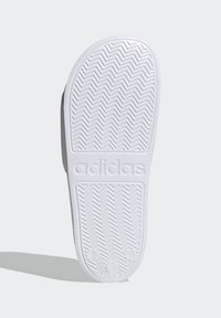 Sola di ciabatta Adidas, caratterizzata da un motivo a zigzag in gomma bianca e logo in rilievo. Parte superiore grigia liscia. Forma piatta e arrotondata.