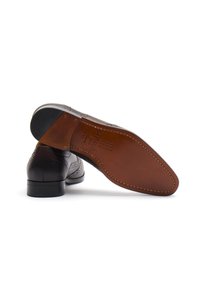 Hnědé kožené boty s brogue detaily, které mají hladký povrch a kontrastní tmavou podrážku. Šité akcenty zdůrazňují design.