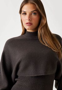 Pull à col roulé en tricot côtelé gris foncé, présentant une coupe décontractée et des manches longues, avec un tissu texturé et un col haut.