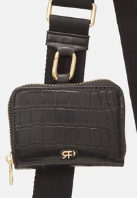 Portefeuille en cuir noir embossé crocodile avec une fermeture éclair dorée et un logo attaché à une sangle en tissu noir équipée d'un clip en métal doré.