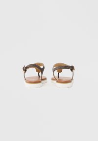 Hnědé kožené sandály s hladkou texturou, vybavené zadním páskem, zapínáním na kotníku a plochou bílou podrážkou.