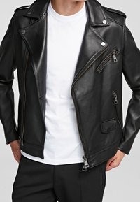 Svart lädermotorcykeljacka med en sned krage, asymmetrisk dragkedja, dragkedjeficka på bröstet och sidfickor. Bärs över en vit skjorta.