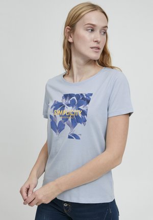 Camiseta de algodón azul claro con un gráfico floral en tonos azules y el texto "LA SIMPLICIDAD HECHA PERFECTA" en amarillo. Diseño clásico de cuello redondo.