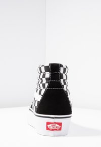 Schwarz-weißer karierter High-Top-Sneaker aus Wildleder und Canvas-Materialien, mit weißen Nähten und einem roten "Vans Off The Wall"-Logo an der Ferse.