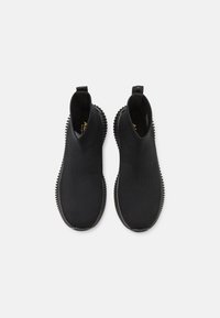 Schwarze Slipper mit strukturiertem Obermaterial, elastischen Seiteneinsätzen und einer robusten Gummisohle mit runden Erhebungen für besseren Halt.