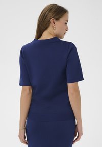 Pull polo bleu marine manches courtes avec col et ourlet côtelés. Le tissu semble légèrement texturé avec des détails subtils.