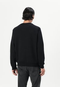 Svart sweatshirt med rund halsringning, långa ärmar och ribbade ärmslut. Mjukt tyg och avslappnad passform, bärs tillsammans med grå denimbyxor.