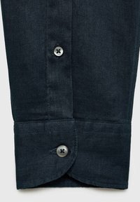 Puño de camisa azul oscuro hecho de tela texturada, con un borde redondeado y dos botones con cuatro agujeros cada uno para abrochar.
