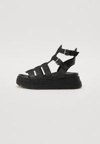 Sandale platform din material sintetic, de culoare neagră, cu mai multe curele și catarame ajustabile. Talpă groasă cu un model texturat.