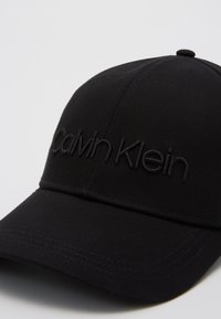 Casquette noire en coton avec une visière incurvée et logo Calvin Klein brodé dans un fil noir assorti. Tissu texturé avec un design structuré.