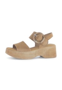 Sandales à plateforme en suède beige avec de larges bandes et un détail de boucle circulaire. La semelle est épaisse, en bois, avec une finition texturée.