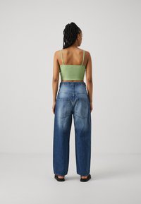 Zöld csíkos crop top vékony pántokkal, laza szabású, halványkék, bolyhos farmer nadrággal, hátul zsebekkel. Egyszerű, hétköznapi stílus.