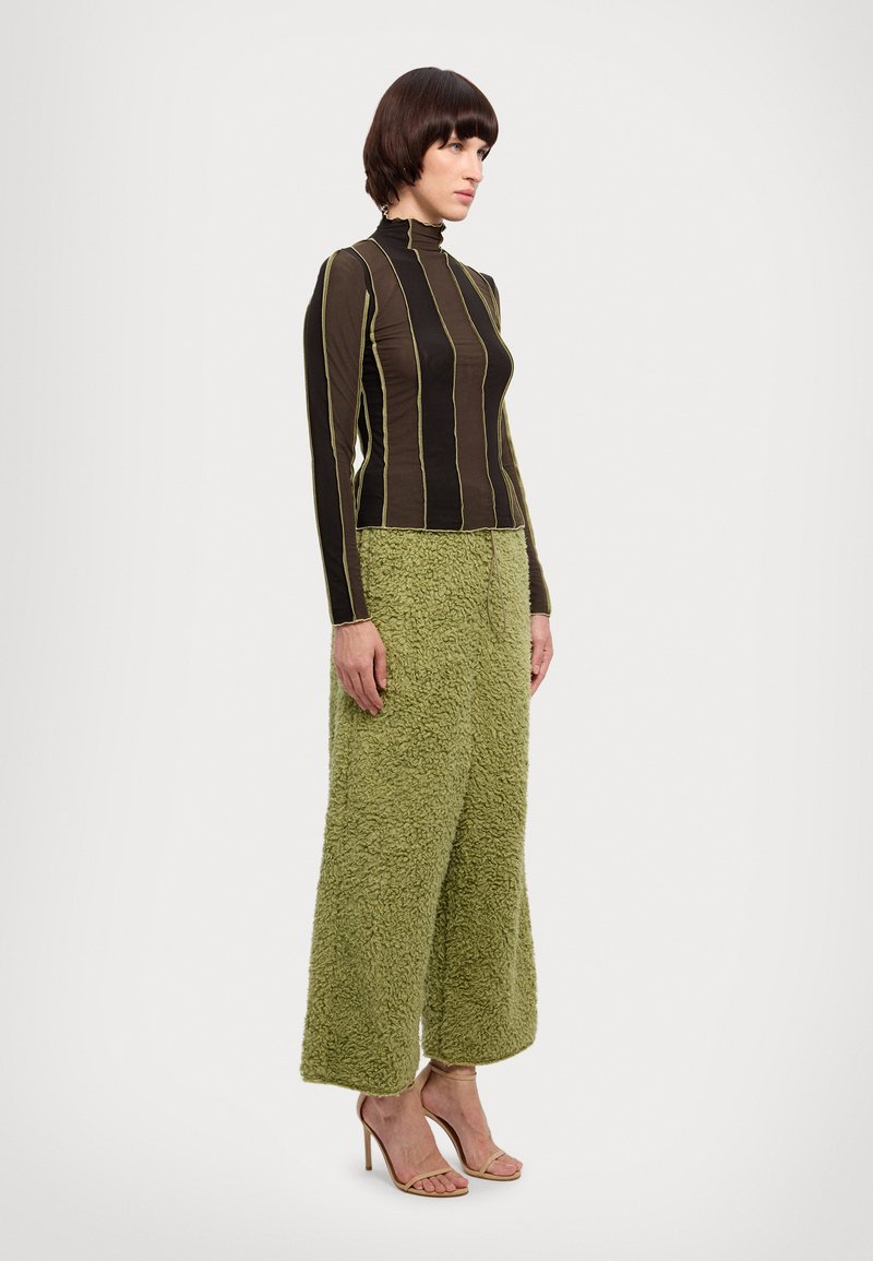 Haut à manches longues rayé marron avec col montant ; associé à un pantalon large en peluche vert clair. Le mannequin porte des talons nus à lanières.