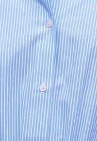 Υφασμα με κάθετες ρίγες σε μπλε και άσπρο, με δύο στερεωμένα λευκά κουμπιά κατά μήκος ενός ραμμένου πατιλέτας.