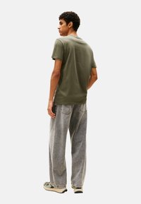 T-shirt in cotone verde oliva con colletto a girocollo, maniche corte e vestibilità comoda, abbinato a jeans a gamba larga grigi scoloriti e sneakers verdi.