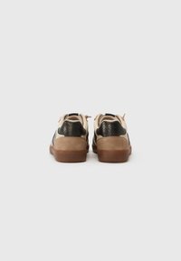 Beige sneakers med sorte slangeskinds mønstrede accenter og en brun gummisål. Har snørre lukning og polstret krave. Minimalistisk design.