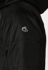 Doudoune noire avec un design matelassé, texture lisse et un petit logo argenté sur la manche gauche.