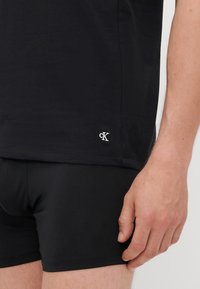 Μαύρο κοντομάνικο βαμβακερό T-shirt με μικρό λευκό λογότυπο "CK" στο τελείωμα, σε συνδυασμό με μαύρη εφαρμοστή βερμούδα. Λείος υφασμάτινος. 